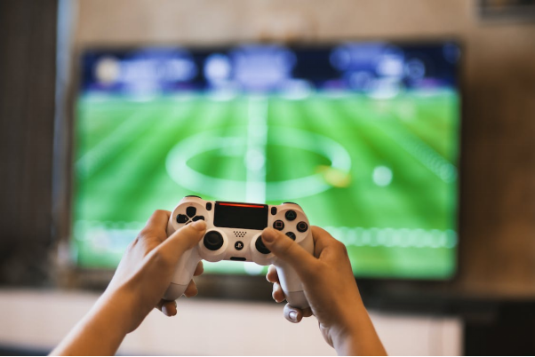 A person is holding a controller in front of a screen showing a football field